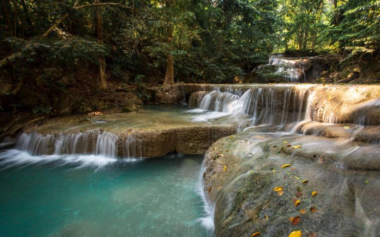 Tranquil waterfall cascading over rocks in lush Erawan National Park.