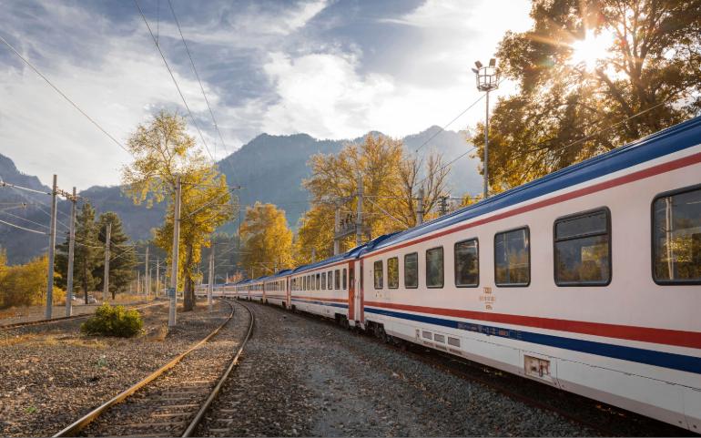 A picturesque train travels through a vibrant autumn landscape with mountains