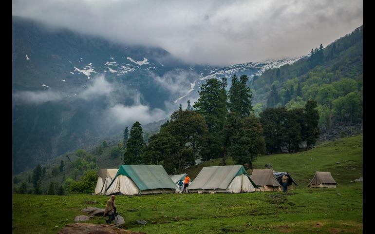 amping in a serene mountain landscape with tents, trees, and cloudy sky.
Image Credit - Guduru Ajay bhargav/Pexels