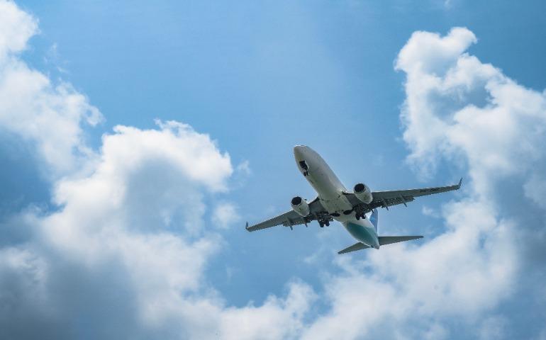An Airplane soars in the sky with white clouds and blue backdrop