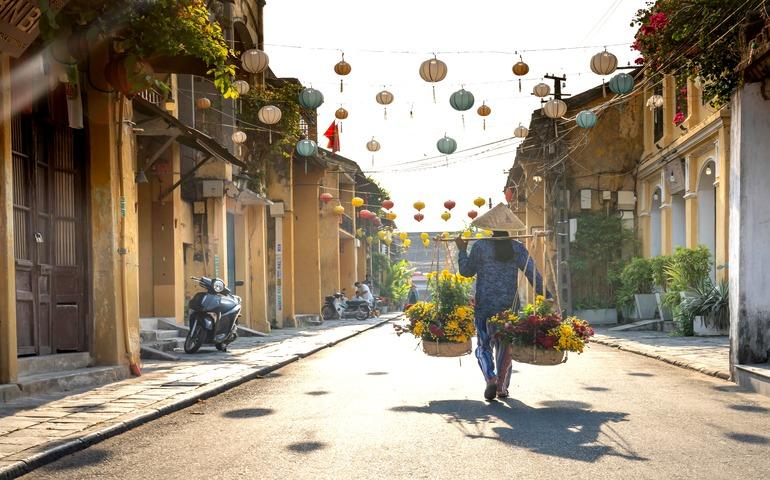 A woman in traditional attire walks with flowers in Hội An's vibrant streets.
Image Credit: Quang Nguyen Vinh/Pexels