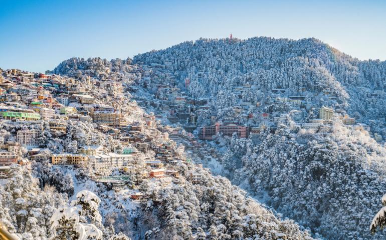 A scenic view of Shimla in winter, with snow-covered buildings and forests under a clear blue sky.
Image Credit - shalender kumar/Unsplash