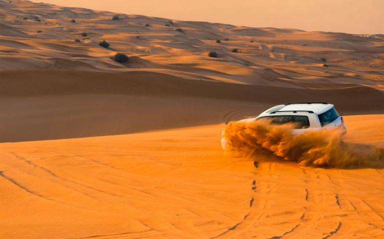 A thrilling SUV driving through the sand dunes of Dubai's desert landscape at sunset.
Image Credit: Stephane Hurbe/Pexels