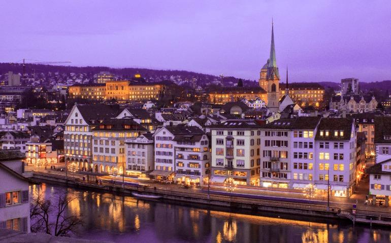 Stunning cityscape of Zurich at twilight with illuminated buildings and a serene river view.
Image Credit: Susanna Marsiglia/Pexels