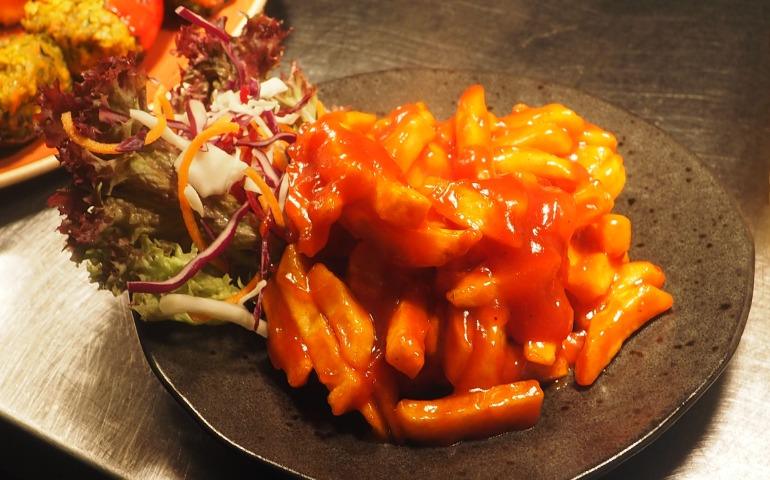 Plate of spicy Korean tteokbokki paired with a fresh vegetable salad.
Image Credit: Chan Walrus/Pexels