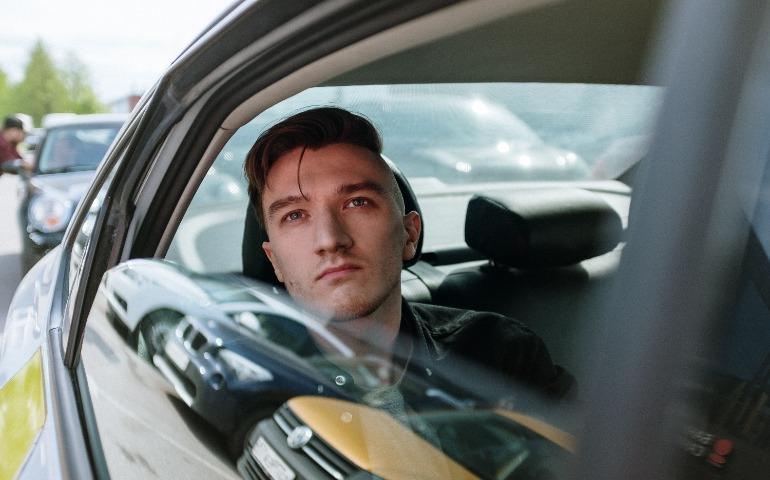 Young man gazes thoughtfully through a taxi window amidst urban traffic, enjoying the ride.
Image Credit: cottonbro studio/Pexels