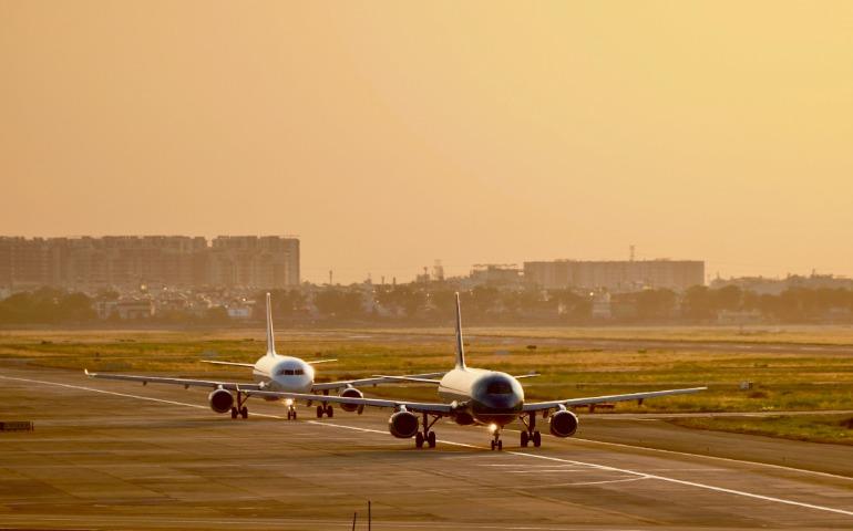 Two commercial airplanes taxiing at sunset with cityscape in background.
Image Credit: Tuan Vy/Pexels